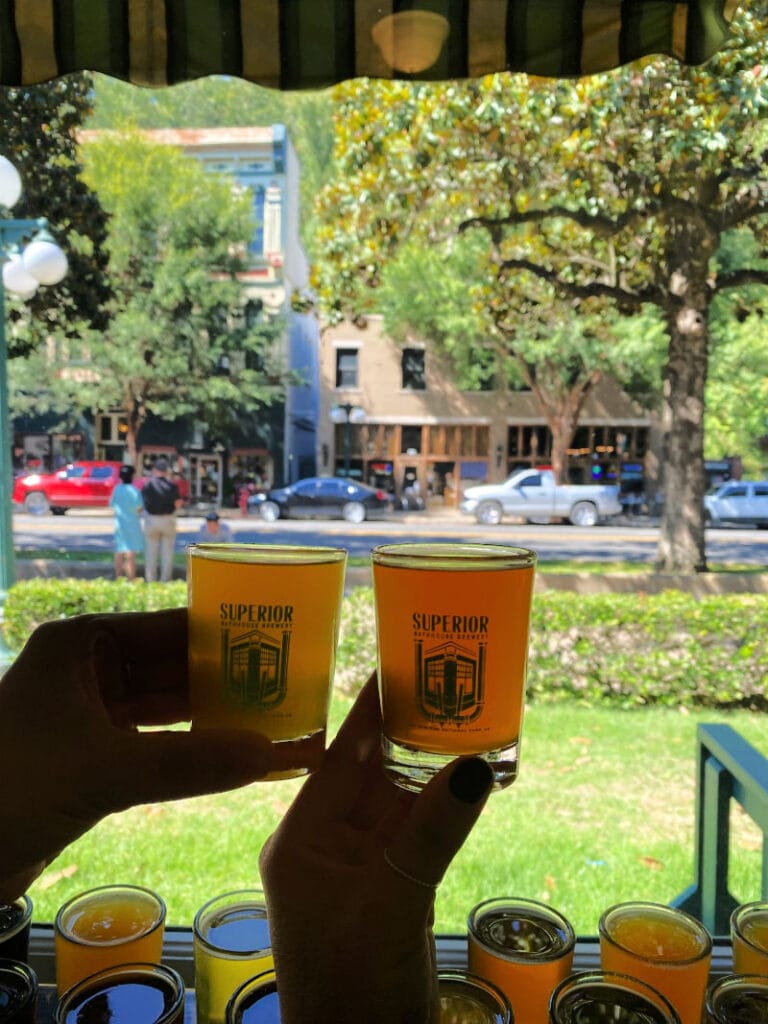 Two hands holding up one beer flight glass against the window
