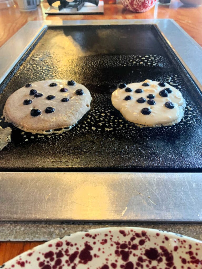 Two blueberry pancakes cooking on the griddle at the table