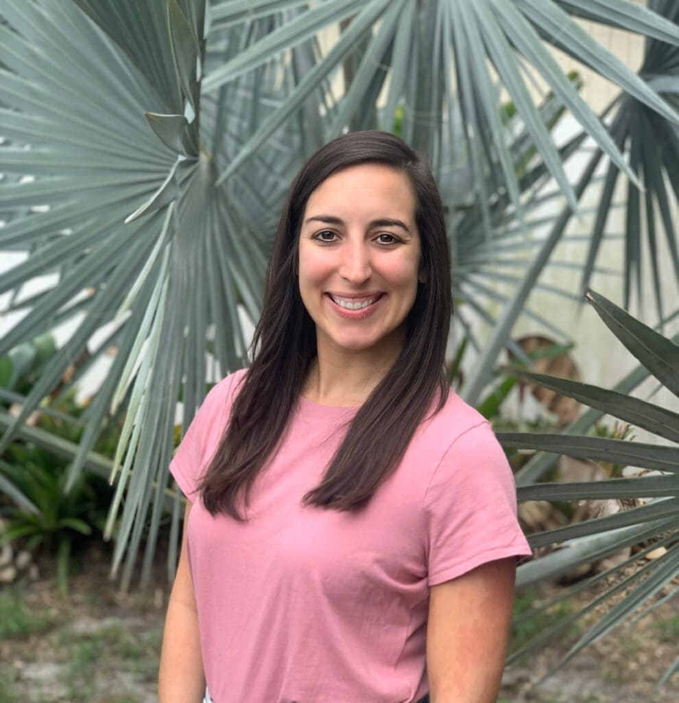 A headshot of me in a pink shirt smiling with palms in the background