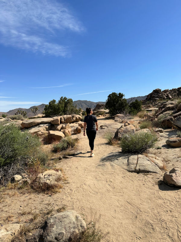 Me walking on a trail in Joshua Tree National Park with various plants and rocks surrounding the trail