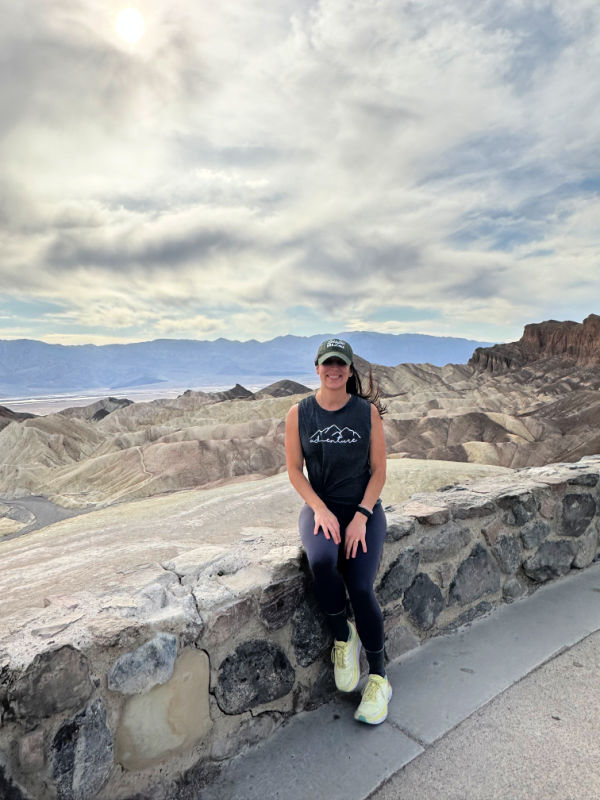 Me sitting on the rock ledge smiling at Zabriskie Point with the mountains in the background